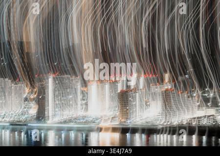 Photo abstraite longue exposition d'un front de mer de la ville la nuit, avec flou de mouvement créant de vastes traînées de lumière sur les gratte-ciel et des reflets sur le calme Banque D'Images