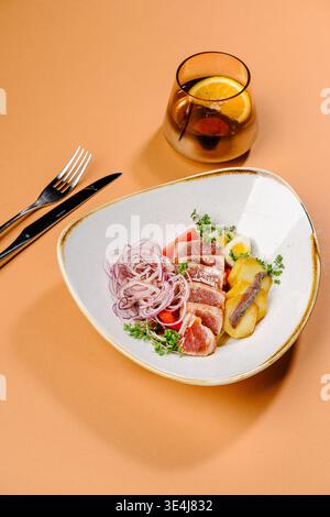 Élégante salade nicoise avec steak de thon poêlé, pommes de terre, œufs de caille, tomates, oignon rouge, anchois et microgreens, arrosé d'huile d'olive, sel et Banque D'Images