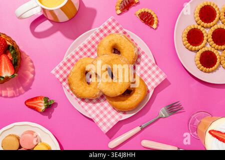 Une scène de petit-déjeuner dynamique avec beignets glacés, biscuits à la confiture de fraises, fraises fraîches, macarons colorés et une boisson rafraîchissante, le tout sur place Banque D'Images