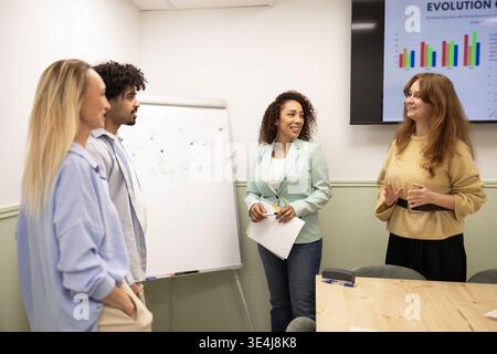 Divers collègues collaborent dans une salle de réunion de bureau moderne, examinant un graphique de croissance à l'écran et discutant de stratégie lors d'une présentation d'équipe i. Banque D'Images