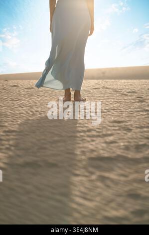 Vue arrière d'une voyageuse anonyme pieds nus vêtue d'une robe légère, debout à la lumière chaude du soleil et contemplant les dunes de Corralejo, Fuerteventura Banque D'Images