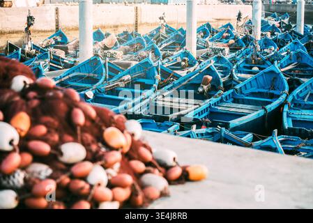 Scène portuaire lumineuse à Marrakech avec de nombreux bateaux de pêche bleus ancrés près les uns des autres, créant une vue sur la marina bondée avec des filets, des bouées et des wa côtiers Banque D'Images