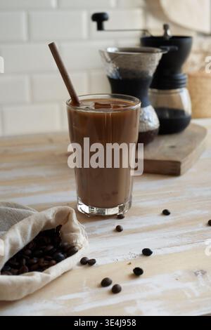 Grand verre de café glacé au chocolat ou de moka rempli de glace et surmonté d'une tête crémeuse mousseuse, servi avec une paille en bois réutilisable sur une languette rustique Banque D'Images