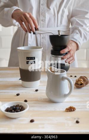 Gros plan des mains à l'aide d'une presse française pour préparer du café frais dans une cuisine minimaliste. Recette maison étape par étape avec moulin, haricots, tasse et pou crémeux Banque D'Images