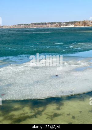 Gros plan d'une grande banquise texturée flottant dans les eaux claires et peu profondes d'un lac turquoise. L'image capture la transition des saisons, Banque D'Images