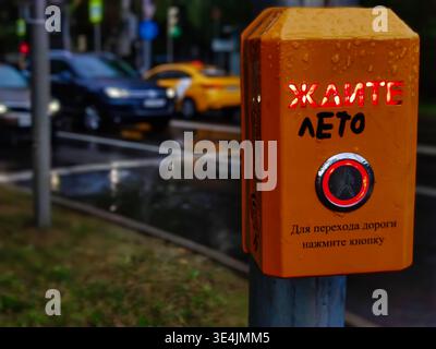 Gros plan d'un bouton de feu de circulation jaune portant le mot rouge « WAIT » et un graffiti manuscrit qui change le sens de « WAIT » Banque D'Images