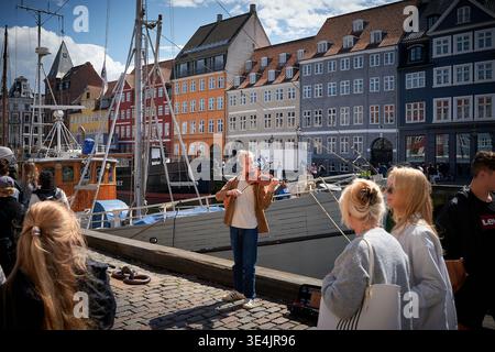 Un homme joue du violon devant une foule de gens. La foule regarde sa performance. Il y a des bâtiments colorés en arrière-plan. Banque D'Images