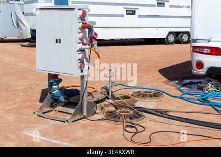 Vue plus large d'une armoire de service électrique portable, fosses à accès ouvert, tuyaux et câbles disposés entre les caravanes temporaires et les logements mobiles U. Banque D'Images