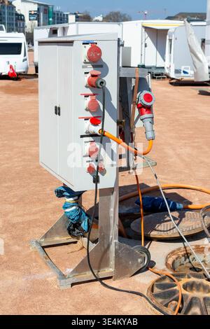 Armoire de raccordement électrique avec prises industrielles et câble orange connecté à côté de fosses ouvertes dans une zone de service temporaire pour caravanes et tr Banque D'Images