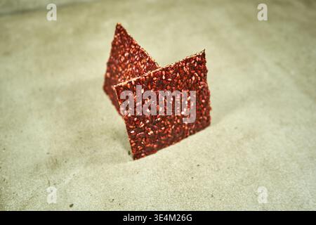 Deux morceaux triangulaires de craquelins rouges ou de cuir de fruits debout dans du sable beige. Les produits alimentaires ont une surface rugueuse et texturée couverte Banque D'Images