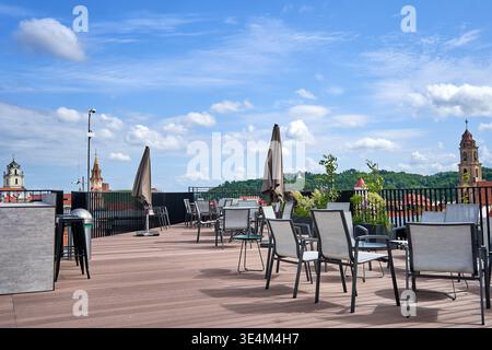 Un toit-terrasse spacieux avec mobilier de jardin moderne comprenant des chaises, des tables et des parasols fermés disposés sur une terrasse en bois. La terrasse Banque D'Images