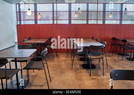 Un intérieur moderne et vide de cafétéria ou de salle à manger arborant un mobilier contemporain. L'espace contient plusieurs tables rectangulaires en bois Banque D'Images