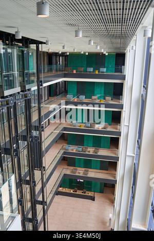 Une vue intérieure en angle élevé d'un atrium moderne d'immeuble de bureaux à plusieurs étages avec ascenseurs en verre sur le côté gauche. Les caractéristiques de l'architecture sont ouvertes Banque D'Images