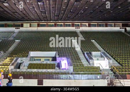 Vue intérieure d'un grand stade ou d'une arène vide avec des rangées de sièges verts disposés en sections étagées séparées par des escaliers en béton. Le plafond Banque D'Images