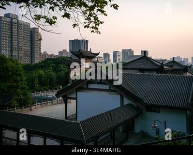 Wuhan, Chine - 19 mai 2025 : cour pavée entourée de passerelles couvertes chinoises traditionnelles avec des toits en tuiles sombres et des murs extérieurs blancs. T Banque D'Images