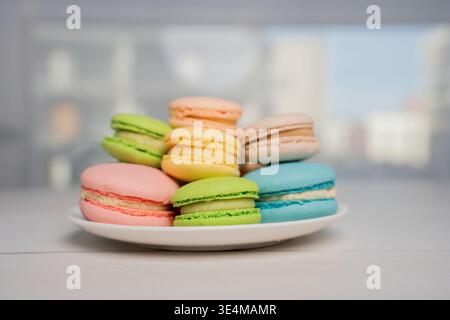 gros plan de macarons pastel empilés sur une plaque blanche au sommet d'une table en bois clair, éclairée par une lumière douce de fenêtre avec une faible profondeur de champ et un b flou Banque D'Images