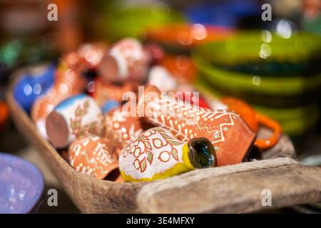 Gros plan de tasses traditionnelles en céramique cuite peintes à la main et de récipients miniatures disposés dans un bol en bois rustique. Les caractéristiques de la poterie sont complexes Banque D'Images
