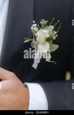 Boutonnière fleurie ornée de fleurs jaunes et blanches, y compris des roses et des marguerites, sur un revers texturé. Parfait pour les mariages et les événements formels à Banque D'Images