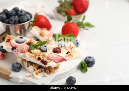 Morceaux d'écorce de yaourt savoureuse avec des baies, granola et menthe sur une table lumineuse, gros plan. Espace pour le texte Banque D'Images