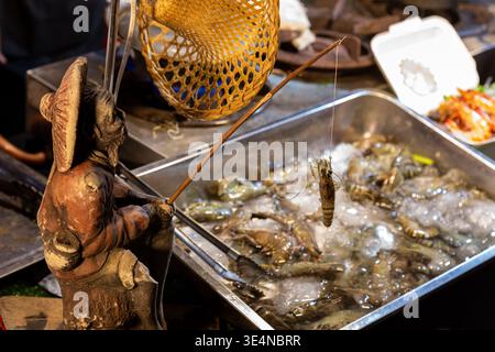 Une figure de pêcheur tient une crevette au-dessus d'un plateau rempli de crevettes reposant sur de la glace pilée. Banque D'Images