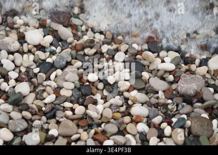 Galets sur une plage avec des vagues éclaboussant au coucher du soleil Banque D'Images