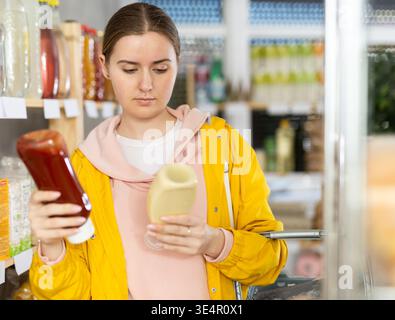 Jeune femme choisissant des sauces dans le magasin Banque D'Images