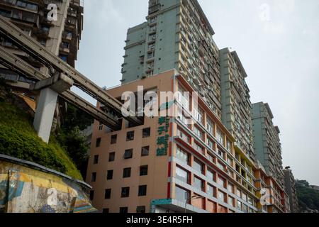 Immeubles urbains de grande hauteur aux façades colorées. Des voies aériennes traversent une pente raide. La verdure pousse à côté des structures en béton. Altéré Banque D'Images