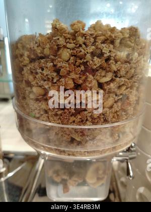 Distributeur de granola rempli d'ingrédients de granola mélangés, y compris l'avoine, les noix et les graines, placé dans un cadre de style buffet pour les options de petit-déjeuner Banque D'Images