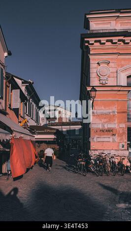 Pittoresque rue étroite à Cesenatico, en Italie, avec le bâtiment historique du marché aux poissons de 1911, des vélos stationnés et une piétonne. Banque D'Images