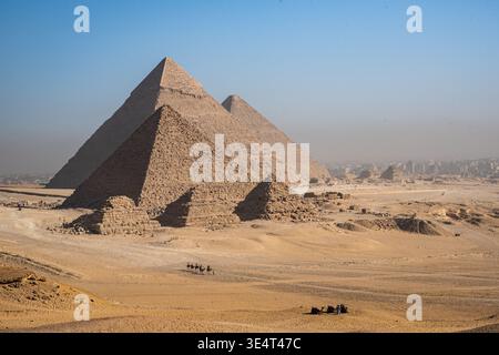 Vue panoramique sur les grandes pyramides de Gizeh et les petites pyramides sur le plateau, avec une caravane de chameaux dans le désert sous un ciel clair Banque D'Images