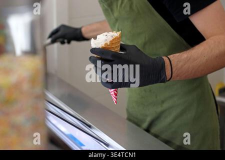 Ouvrier tenant un cône de crème glacée avec garniture au comptoir dans le café. Scène de service alimentaire pour la préparation de desserts, le travail de détail, le service de collation sucré et profes Banque D'Images