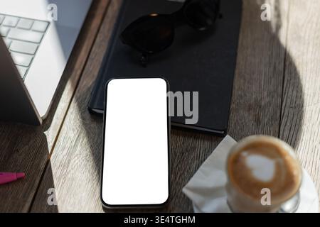 Vue de dessus du smartphone avec écran vide, tasse à café, ordinateur portable et ordinateur portable sur une table en bois. Espace de travail moderne pour le travail à distance ou des projets créatifs. M Banque D'Images