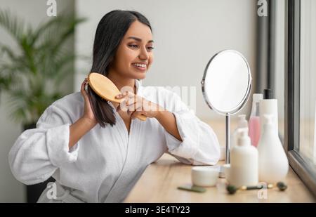 Joyeuse femme indienne peignant de beaux cheveux longs sombres à la salle de bain Banque D'Images