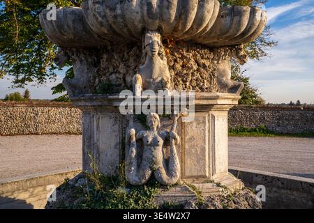 Gros plan d'une ancienne base de fontaine décorée d'une figure mythologique bicaudate de sirène et de chevaux de mer. La structure en pierre altérée est capturée Banque D'Images