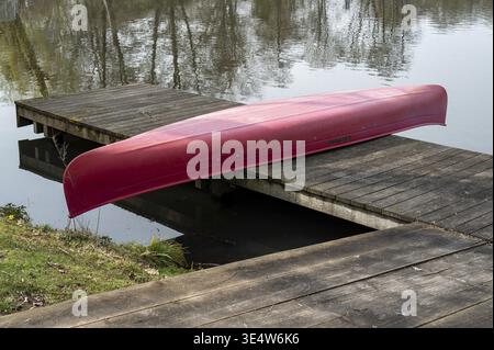 Canoë rouge reposant à l'envers sur un quai en bois à côté de l'eau calme Banque D'Images