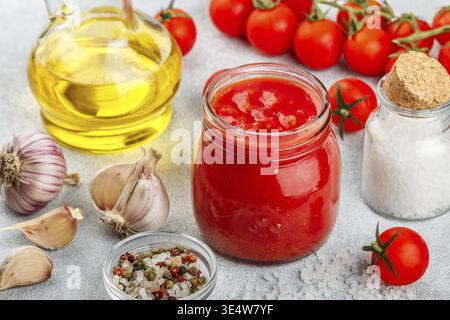 Nourriture, sauce tomate traditionnelle dans un bocal en verre avec de l'ail et des épices. Ingrédients et huile d'olive sur la surface légère. Mise au point sélective Banque D'Images