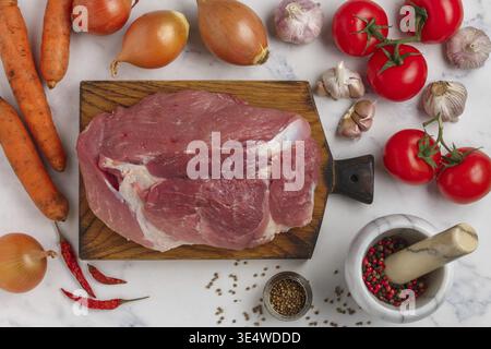 Nourriture, viande de porc crue biologique sur planche à découper et légumes frais (tomates, oignons, ail, carottes, poivrons) sur fond de marbre, épices (coriande Banque D'Images