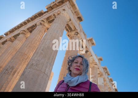 ATHÈNES, GRÈCE - 18 février 2026 : touriste souriante en veste d'hiver violette posant à l'Acropole devant le Parthénon. Banque D'Images