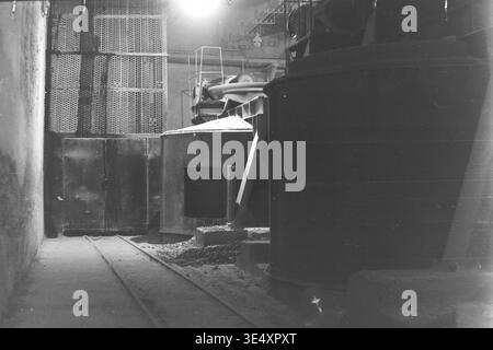 Sloviansk, 1950s-1960s, armature-Insulator Plant (AIZ). Une vue intérieure de l'atelier présentant des cuves de mélange industrielles massives et des systèmes d'engrenages mécaniques lourds utilisés pour traiter l'argile brute et la barbotine liquide pour les isolateurs céramiques. La photographie d'archives en noir et blanc révèle l'échelle monumentale du département de préparation des matériaux, avec de grands réservoirs métalliques, de lourdes poutres de soutien et des voies ferrées au sol. Cette image documente l'ingénierie mécanique soviétique et la puissance industrielle du Donbass pacifique. Banque D'Images