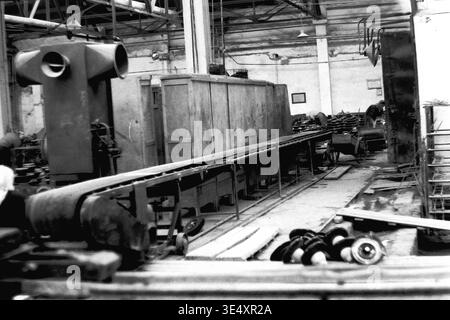 Sloviansk, 1950s-1960s, armature-Insulator Plant (AIZ). Une longue bande transporteuse automatisée s'étend sur l'ensemble de l'usine spacieuse, conçue pour rationaliser le transport des composants céramiques lourds entre les zones de production actives. De grands systèmes de ventilation industriels et des unités d'entraînement mécaniques dominent la zone de travail très fréquentée. Cette perspective architecturale convaincante saisit la modernisation rapide des usines du milieu du siècle, préservant un record inestimable de la vie quotidienne avant la guerre et célébrant l'esprit d'ingénierie d'un Donbass pacifique. Banque D'Images