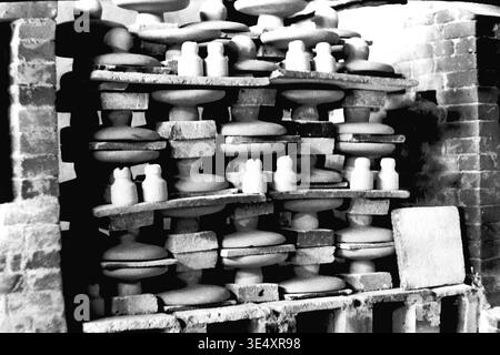 Sloviansk, 1950s-1960s, armature-Insulator Plant (AIZ). Des piles denses d'isolants en céramique brute sont méticuleusement disposées sur des étagères réfractaires lourdes à l'intérieur d'un four à briques industriel massif, prêt pour la cuisson à haute température. L'agencement structurel complexe à plusieurs niveaux maximise l'efficacité de la production tout en assurant une distribution uniforme de la chaleur pour les composants électriques. Cette nature morte architecturale détaillée préserve l'histoire matérielle de la fabrication de masse soviétique, la vie quotidienne avant la guerre et un Donbass pacifique. Banque D'Images