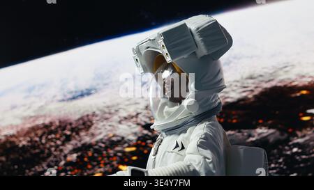 Membre d'équipage souriant de la station orbitale ravi par la beauté de la planète dans l'espace. Femme afro-américaine joyeuse regardant dans la crainte des corps célestes de galaxie pendant l'exploration planétaire, caméra B. Banque D'Images