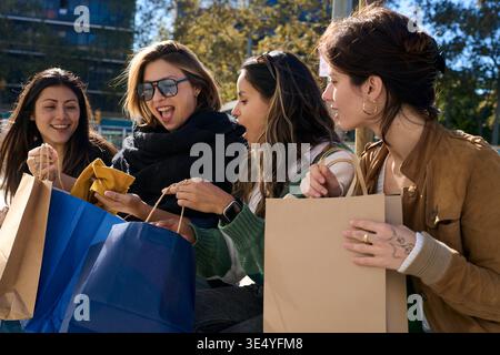 Heureux amis magasinant ensemble ouvrant des sacs à l'extérieur Banque D'Images
