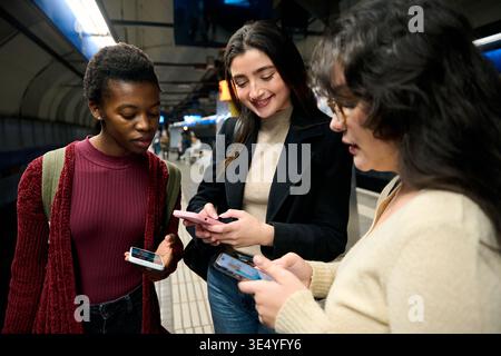 Jeunes femmes diverses utilisant des smartphones dans la station de métro Banque D'Images