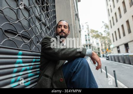 Mode bel homme dans des vêtements décontractés élégants avec manteau assis près du bâtiment à Barcelone Banque D'Images