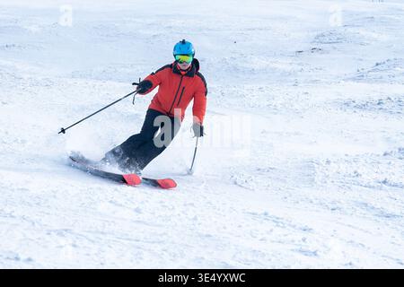 Vue d'un skieur dans une veste orange vibrante et casque bleu sculpte à travers la poudre fraîche, créant un contraste dynamique avec la neige blanche, Val-d Illi Banque D'Images