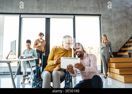 L'image comprend une personne utilisant un fauteuil roulant, représentant l'inclusivité et le travail d'équipe dans un bureau moderne Banque D'Images