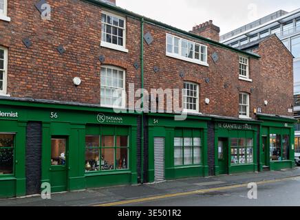 Rangée de bâtiments victoriens en briques rouges avec des façades de magasins peintes en vert assorties sur une rue Northern Quarter, Manchester, Angleterre. Banque D'Images