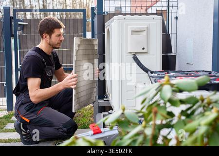 Technicien effectuant l'entretien de la pompe à chaleur extérieure près de l'extérieur du bâtiment résidentiel. Homme installant la pompe à chaleur de source d'air, à l'aide d'outils. Conc Banque D'Images