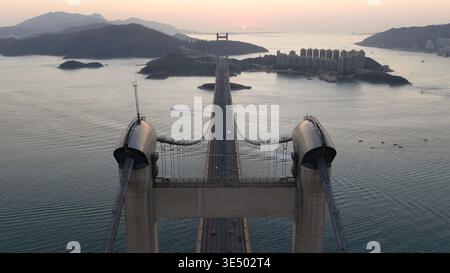 Vue aérienne du pont Tsing ma au coucher du soleil avec le trafic traversant l'eau entre les tours vers des îles lointaines et des immeubles de grande hauteur à Hon Banque D'Images